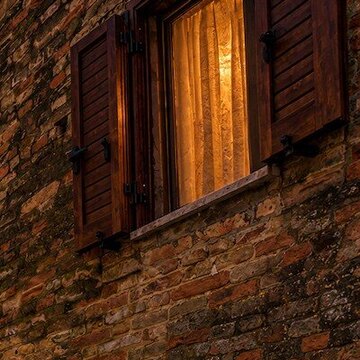 Nachher: dasselbe Fenster mit warm leuchtendem Vorhang, Backsteinwand im Streiflicht